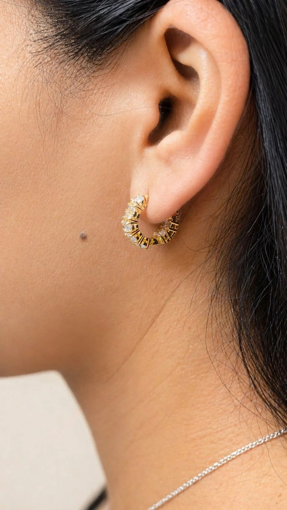 Clear pavé and oval CZ gold huggie hoop earring worn on ear