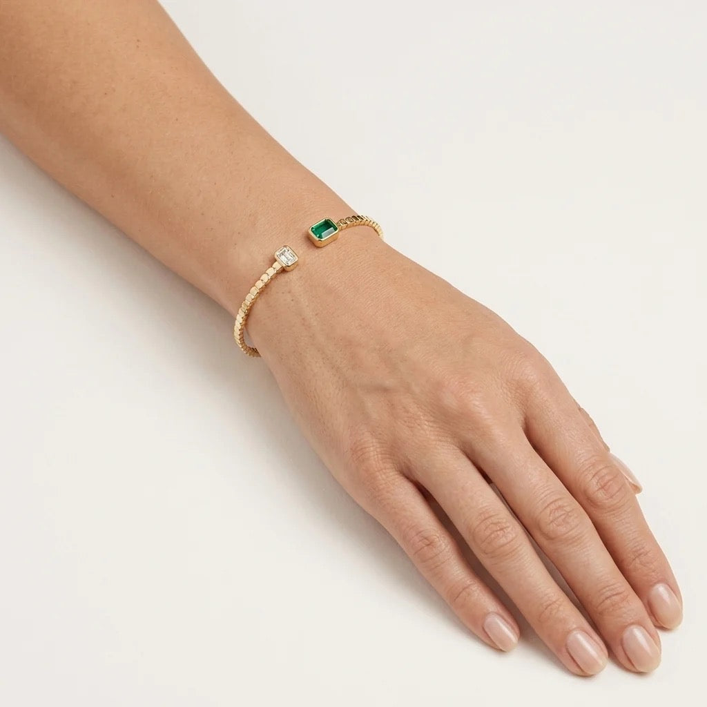 Polished yellow gold emerald open cuff bracelet worn on wrist