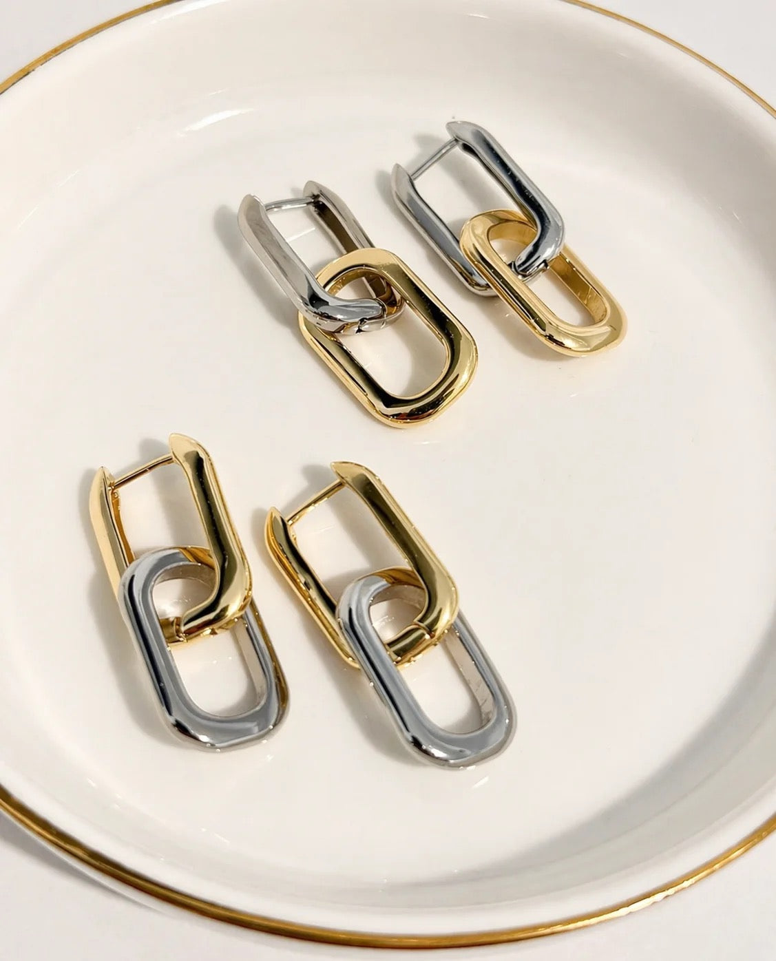 Gold and rhodium two-tone paperclip link earrings styled on a jewelry dish